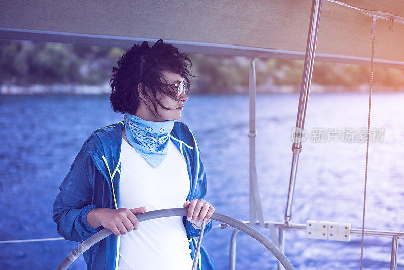 Woman standing behind the sailing wheel on a boat, sailing.